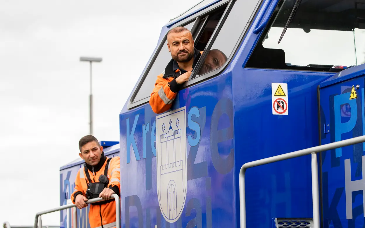 Zwei Lokführer schauen aus einer Lok heraus.