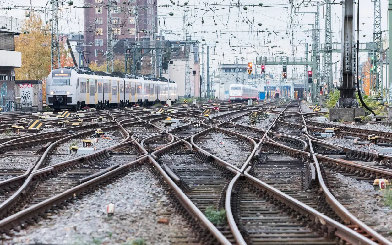 Das Bild zeigt viele Schienen und einen Zug im Hintergrund.