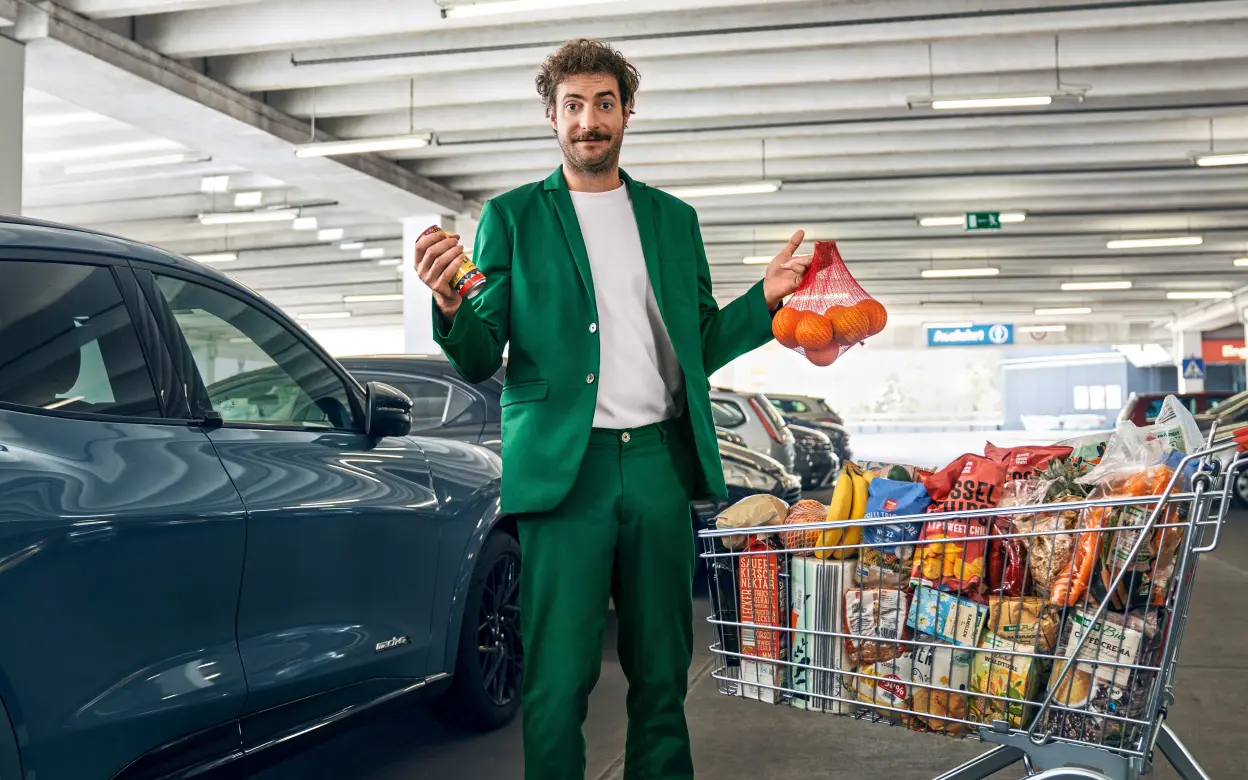 Mann steht mit Einkaufswagen in Parkgarage vor Auto