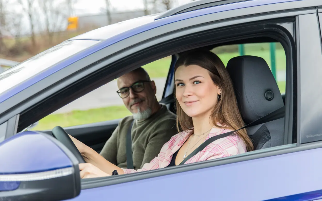 Eine junge Frau sitzt am Steuer, neben ihr sitzt ein Mann.