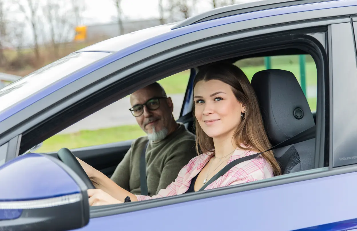 Eine junge Frau sitzt am Steuer, neben ihr sitzt ein Mann.