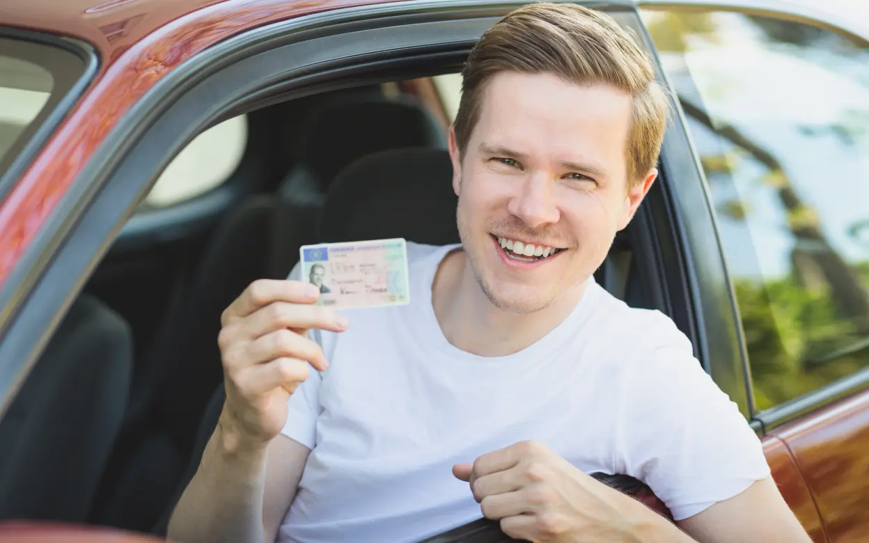 Ein junger Mann zeigt seinen Führerschein in die Kamera.