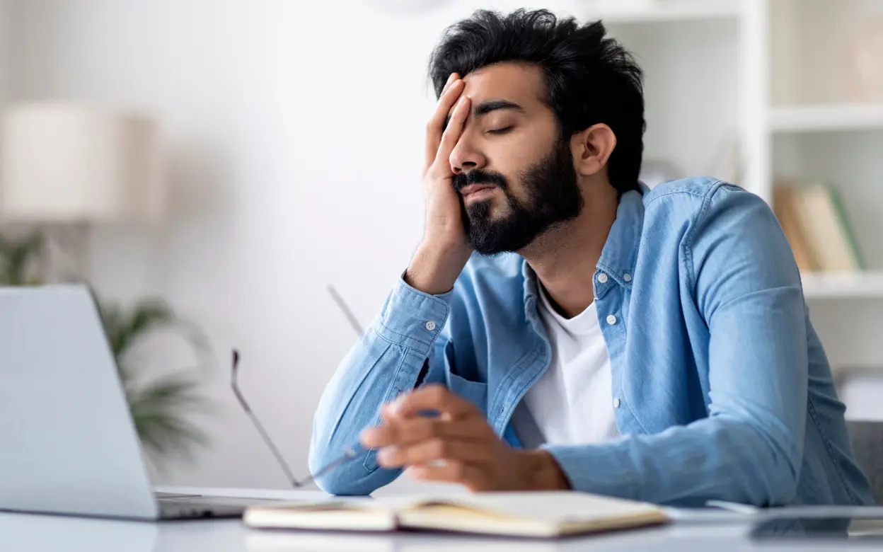 Mann sitzt übermüdet und gestresst am Schreibtisch