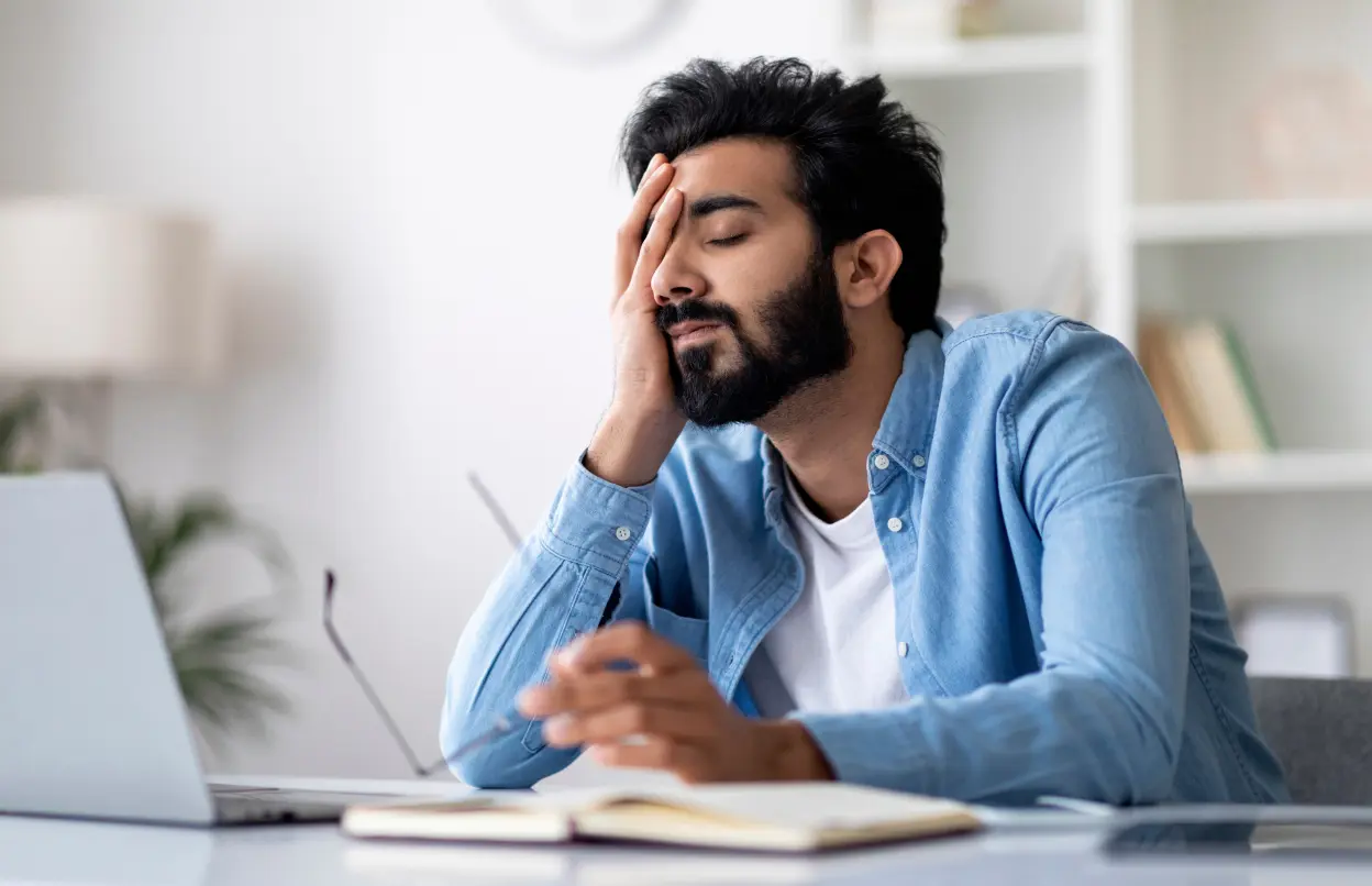 Mann sitzt übermüdet und gestresst am Schreibtisch
