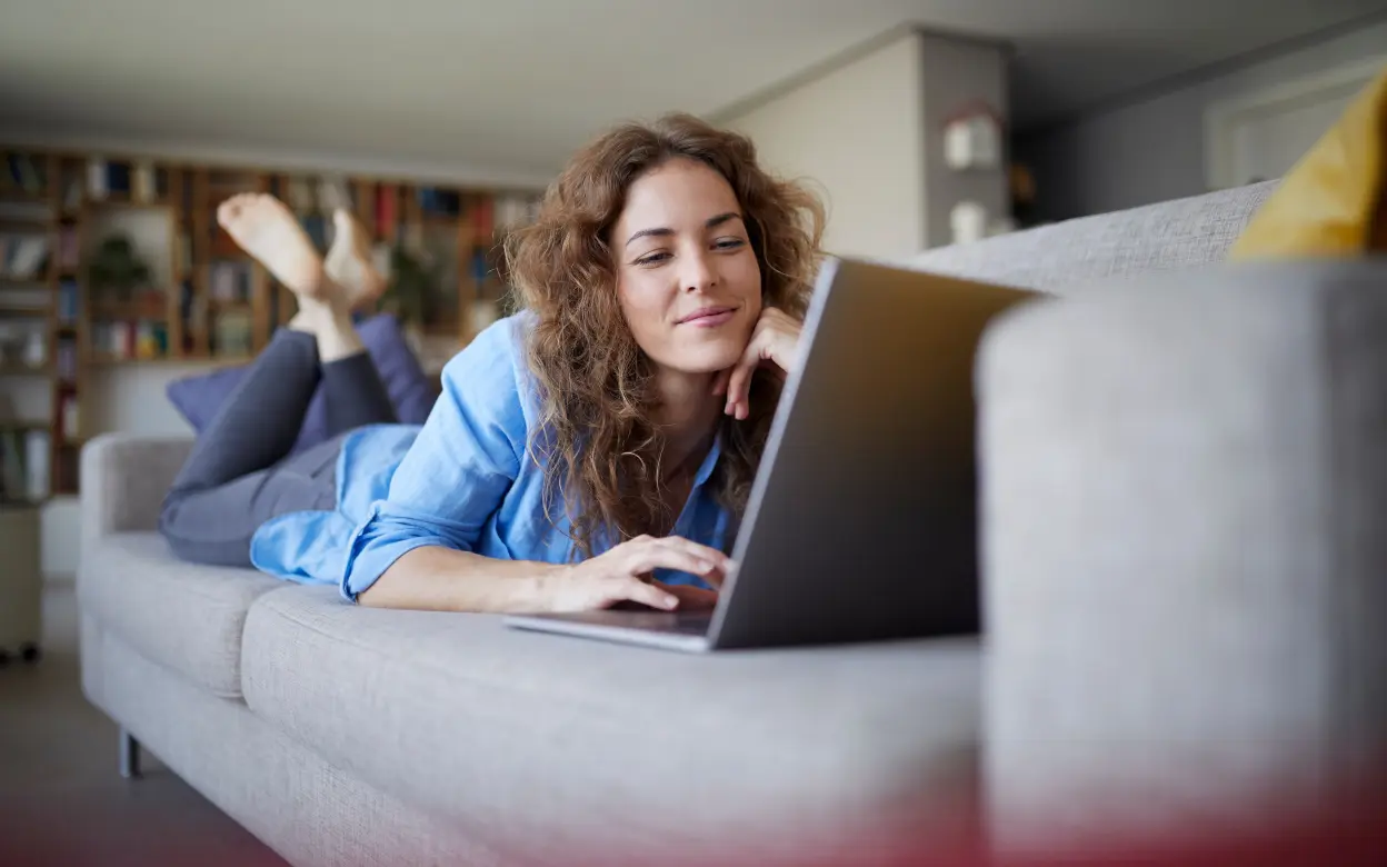 Frau liegt auf Sofa und nutzt ein Laptop
