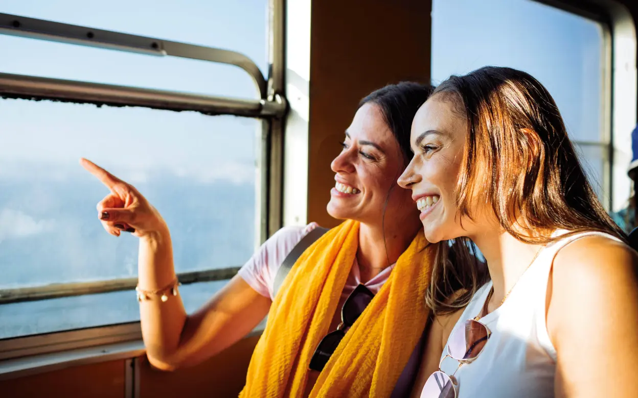 Zwei glücklich lächelnde junge Frauen schauen gemeinsam aus dem Fenster