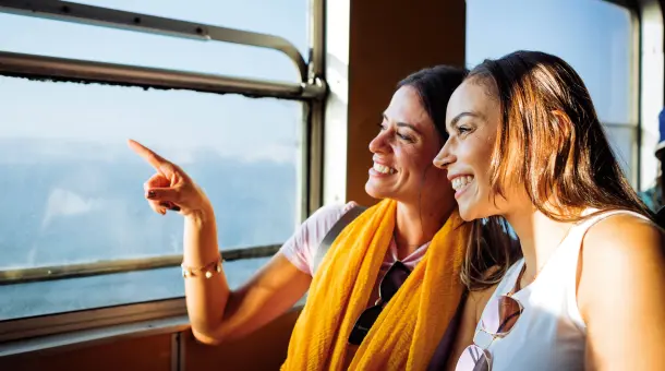 Zwei glücklich lächelnde junge Frauen schauen gemeinsam aus dem Fenster