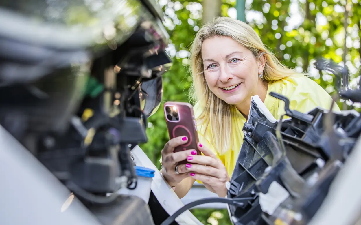 Frau fotografiert Motor eines E-Autos mit Smartphone