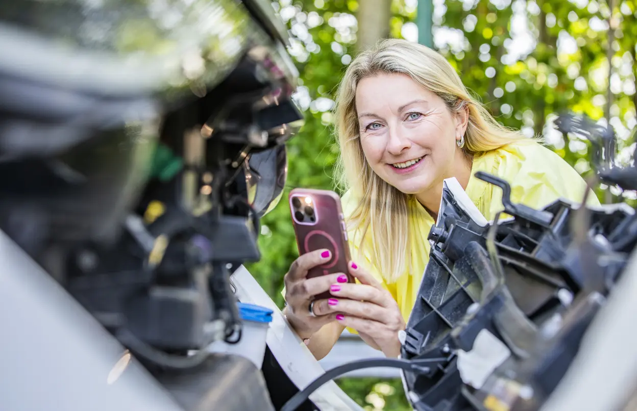Frau fotografiert Motor eines E-Autos mit Smartphone