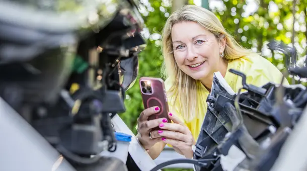 Frau fotografiert Motor eines E-Autos mit Smartphone