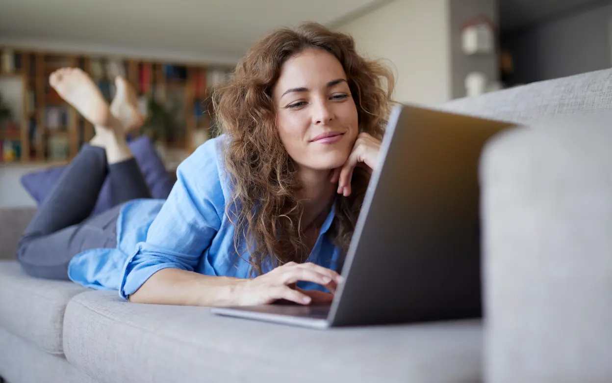 Frau liegt mit Laptop auf dem Sofa 