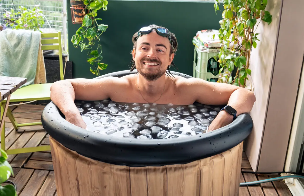 Ein Mann sitzt zufrieden lächelnd in einer Eistonne