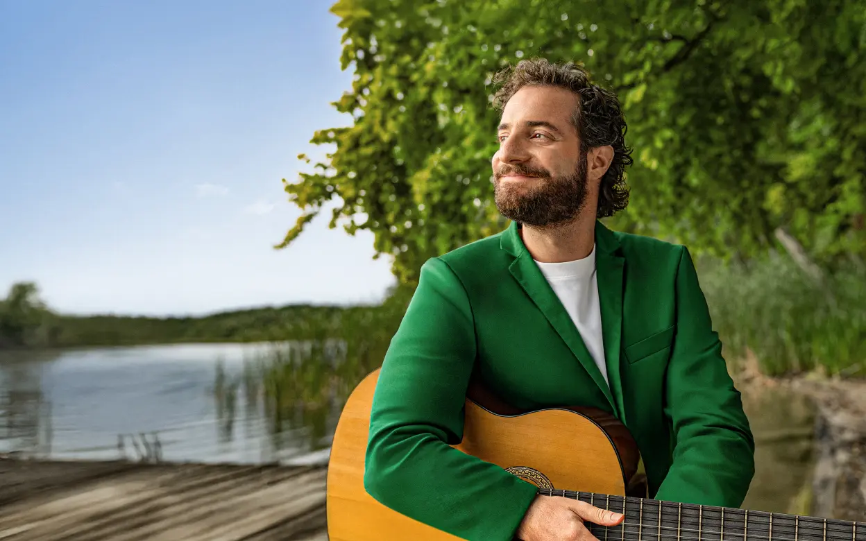 Ein Mann schaut lächelnd zur Seite und hält eine Gitarre