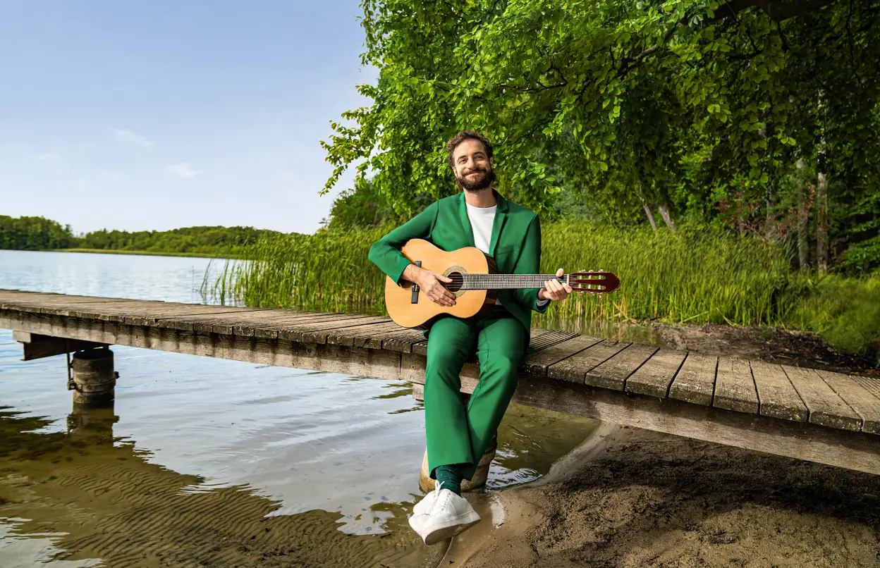 Ein Mann sitzt am See und spielt Gitarre