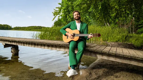 Ein Mann sitzt am See und spielt Gitarre