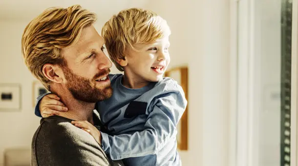 Mann hält Kind im Arm und schaut mit ihm aus dem Fenster