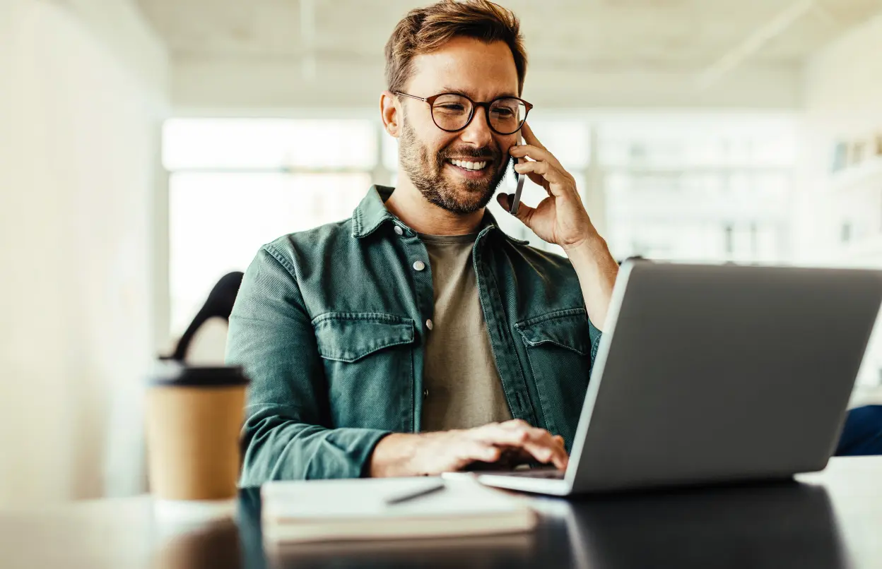 Telefonierender Mann sitzt lächelnd am Laptop