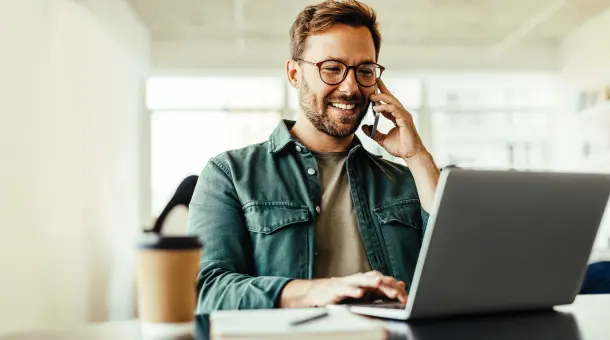 Telefonierender Mann sitzt lächelnd am Laptop