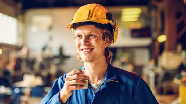 Ein zufrieden lächelnder Arbeiter mit Helm in einer Halle