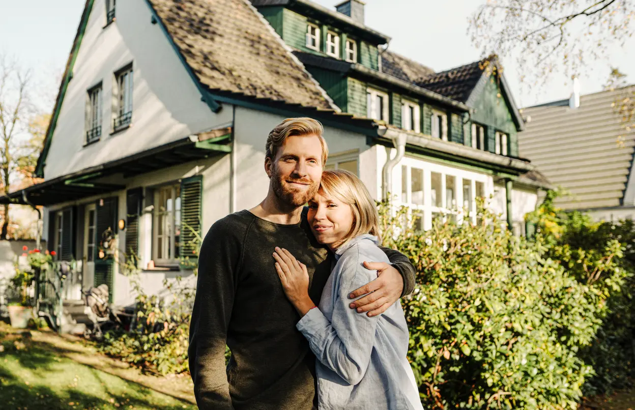 Ehepaar umarmt sich im Garten ihres Eigenheims