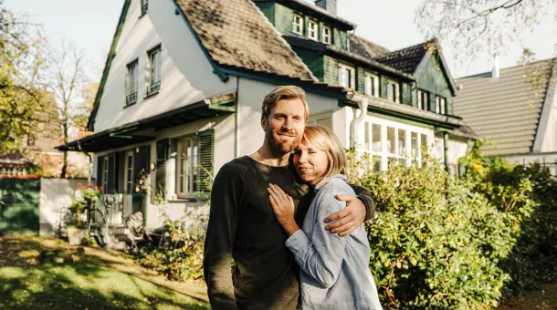 Ehepaar umarmt sich im Garten ihres Eigenheims