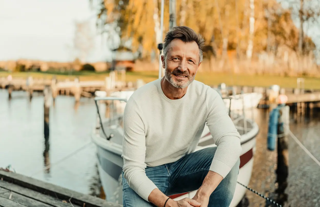 Ein Mann sitzt fröhlich an einem Hafen mit Booten.