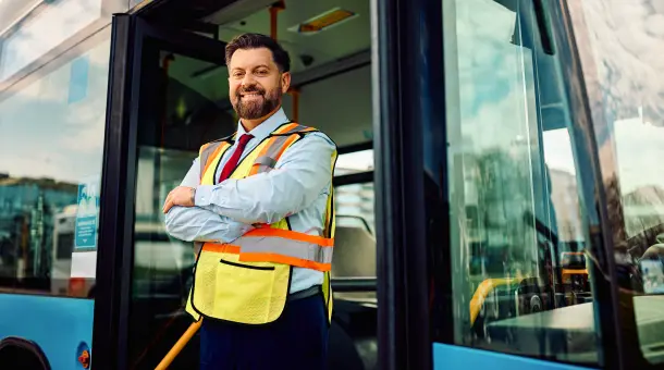 Ein fröhlicher Busfahrer steht vor einem Bus.