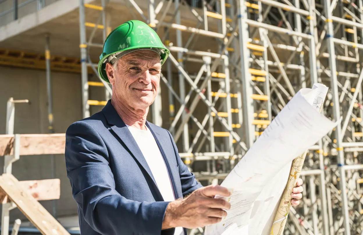 Ein Architekt steht vor einem Neubau und hält einen Plan in der Hand.