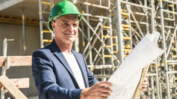 Ein Architekt steht vor einem Neubau und hält einen Plan in der Hand.