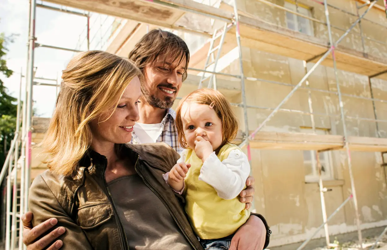 Eine Familie steht lächelnd vor einem eingerüsteten Haus.