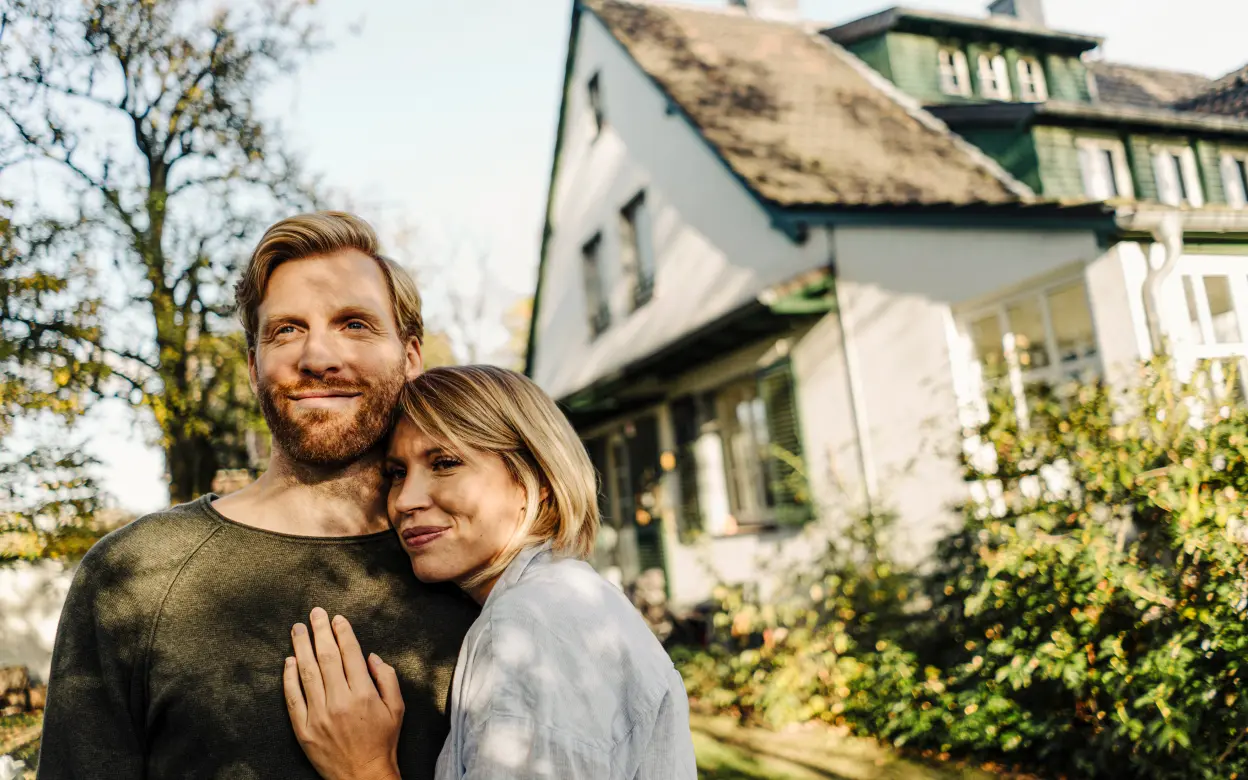 Ein glückliches Paar steht im Garten vor einem Haus.