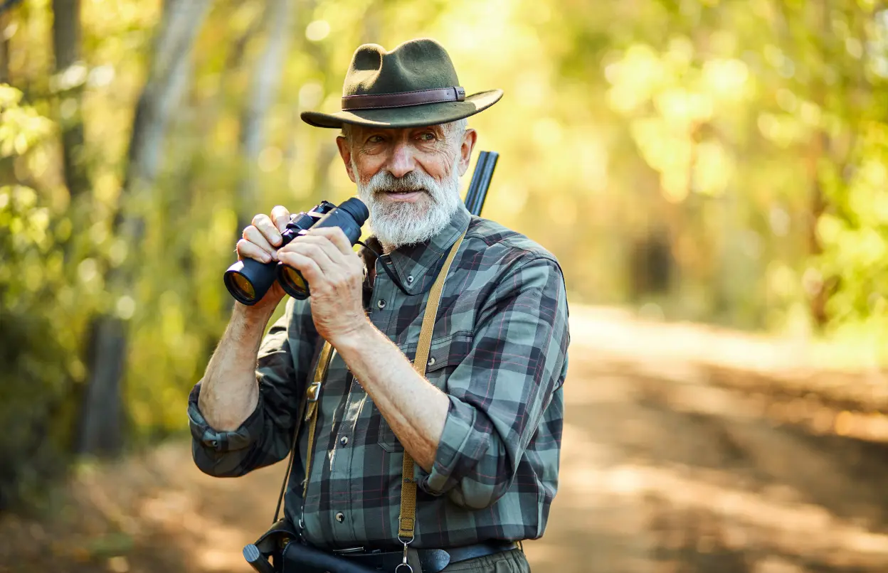 Ein Jäger steht im Wald und hält ein Fernglas in den Händen.