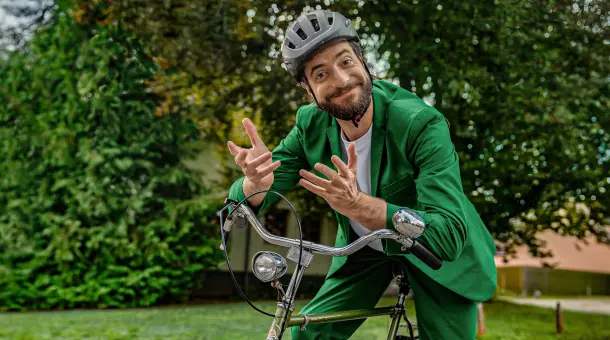 Ein Mann sitzt auf einem Fahrrad und schaut den Betrachter fragend und zugleich freundlich einladend an.