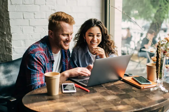 Mann und Frau schauen lächelnd auf einen Laptop