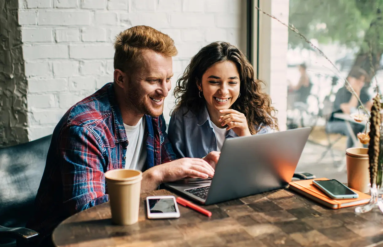 Mann und Frau schauen lächelnd auf einen Laptop