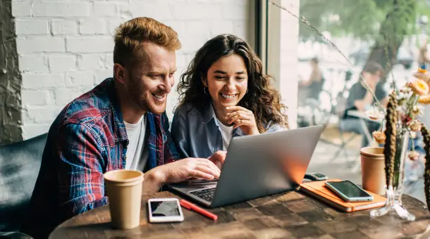 Mann und Frau schauen lächelnd auf einen Laptop