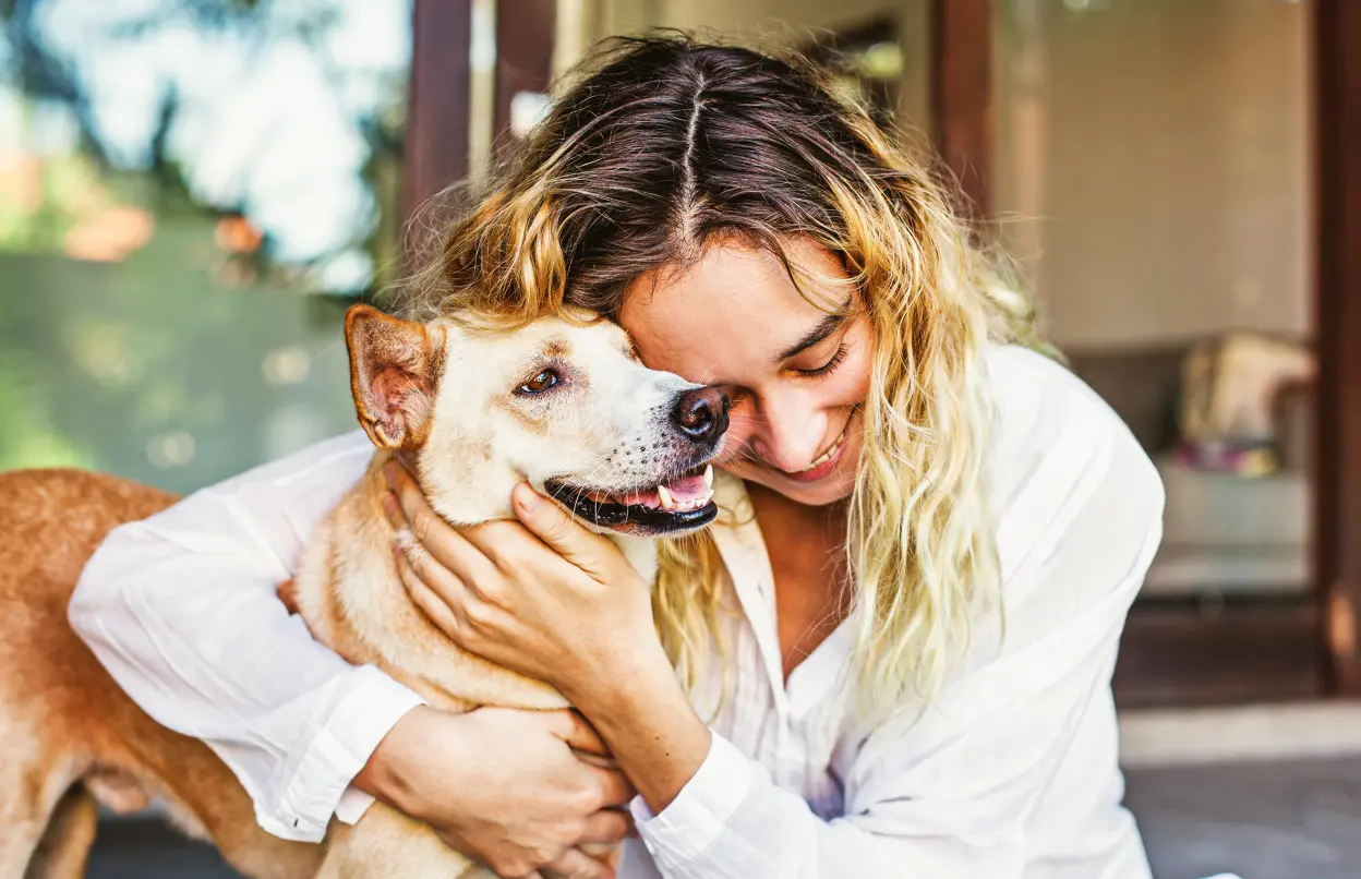 Eine Frau umarmt lachend einen Hund.
