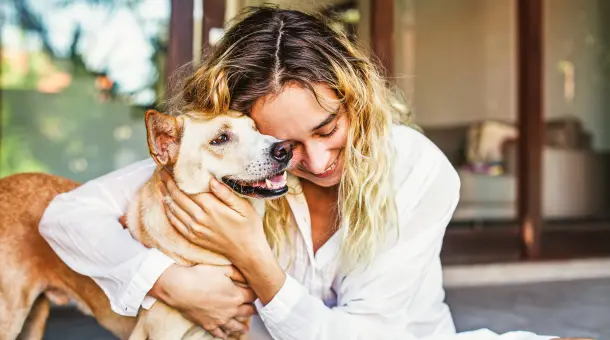Eine Frau umarmt lachend einen Hund.