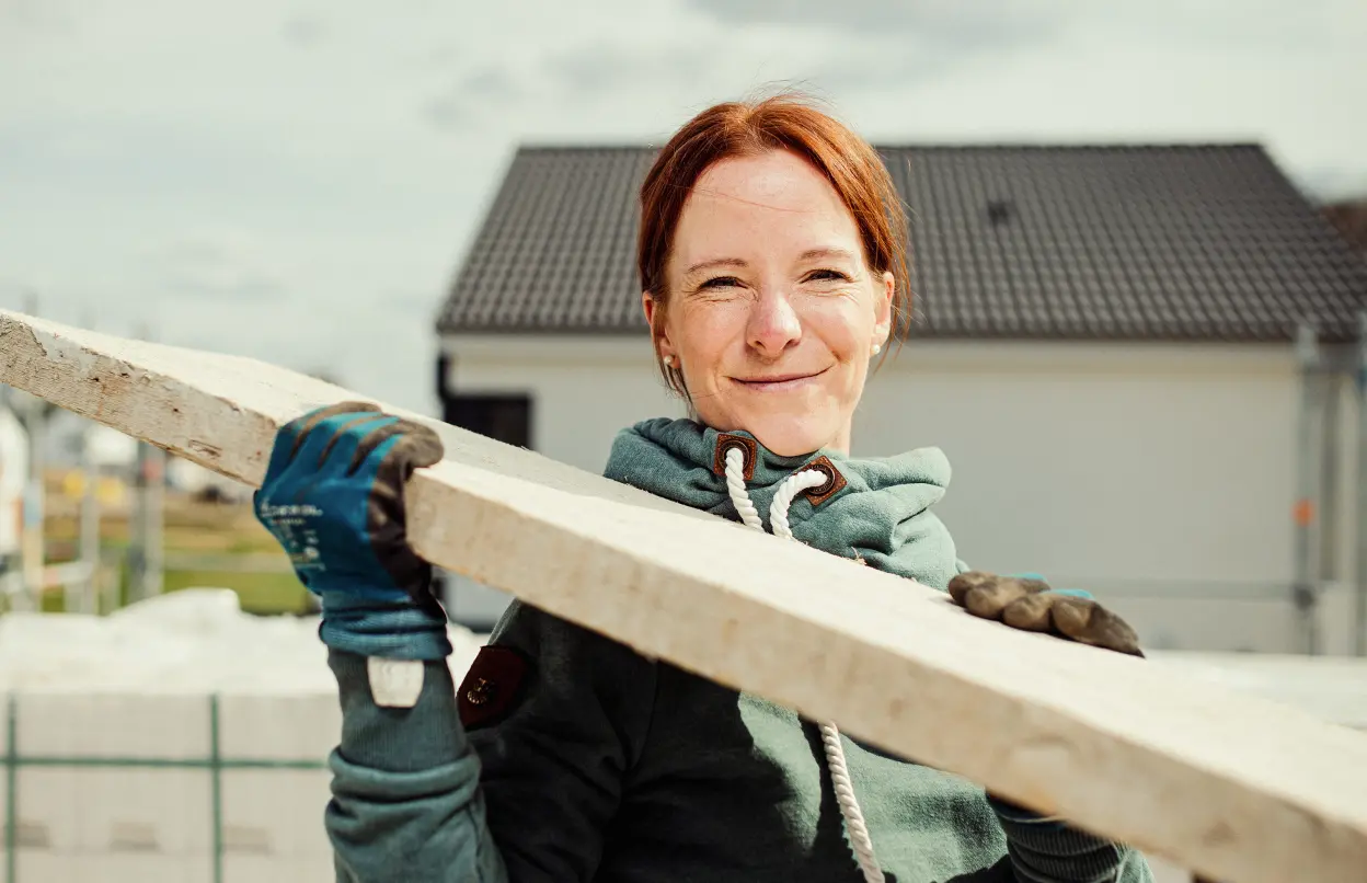 Frau trägt Holzbalken auf Baustelle