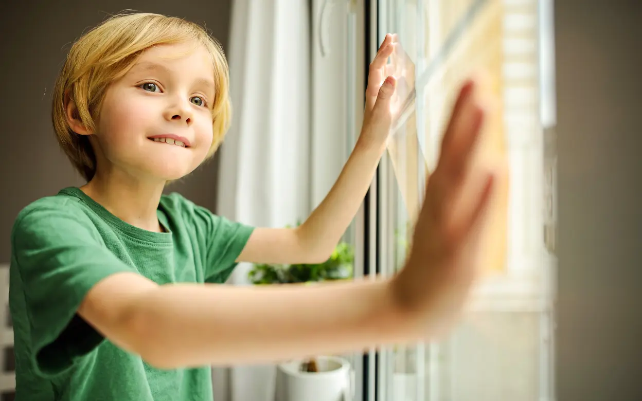 Ein Kind hat die Hände auf ein Fenster gelegt und schaut erwartungsvoll nach draußen.