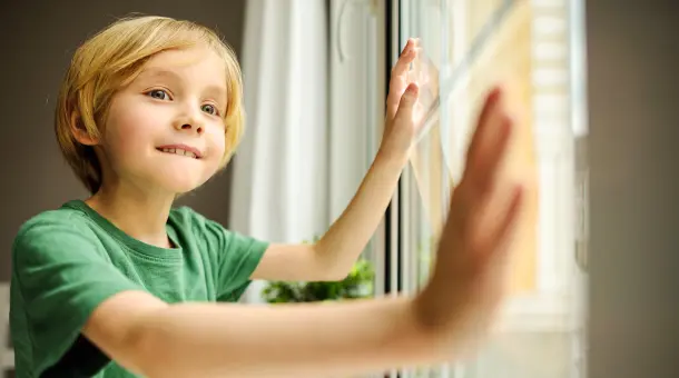 Ein Kind hat die Hände auf ein Fenster gelegt und schaut erwartungsvoll nach draußen.