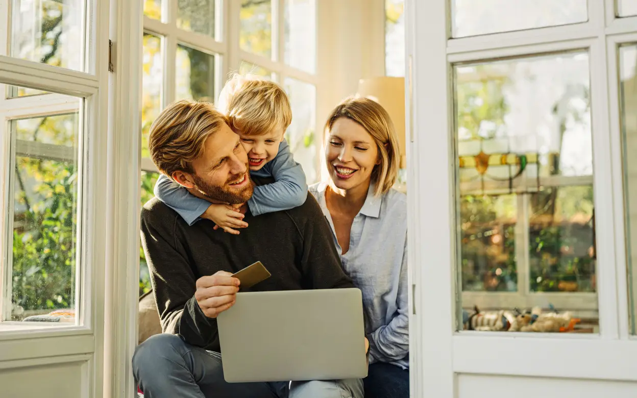 Eine Familie sitzt in einem Wintergarten mit einem Laptop auf dem Schoß.