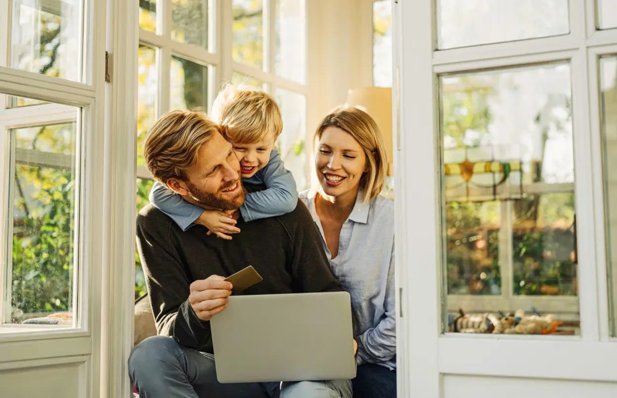 Eine Familie sitzt in einem Wintergarten mit einem Laptop auf dem Schoß.