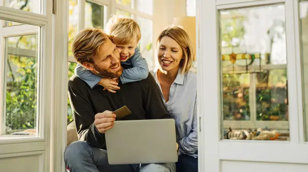 Eine Familie sitzt in einem Wintergarten mit einem Laptop auf dem Schoß.