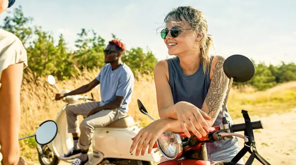 Drei Personen sitzen lächelnd auf Kleinkrafträdern.