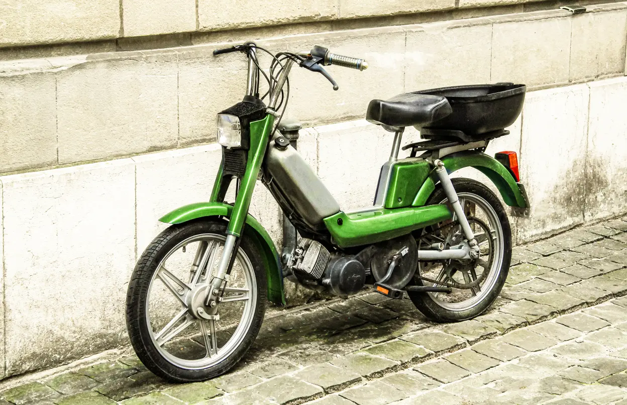 Ein grünes Mofa steht vor einer Wand.