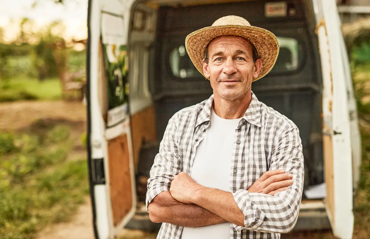 Ein freundlicher Mann mit einem Strohhut steht vor einem Lieferwagen.