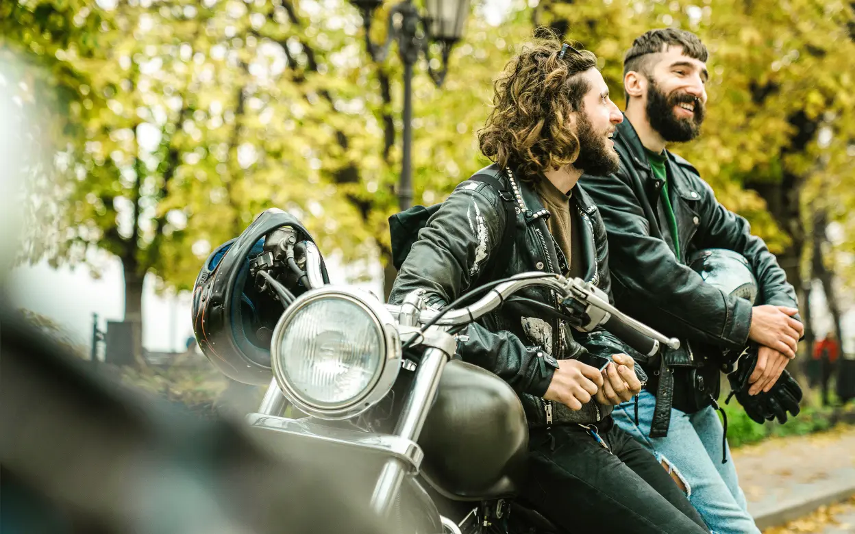 Zwei lachende Motorradfahrer lehnen an einem Motorrad.