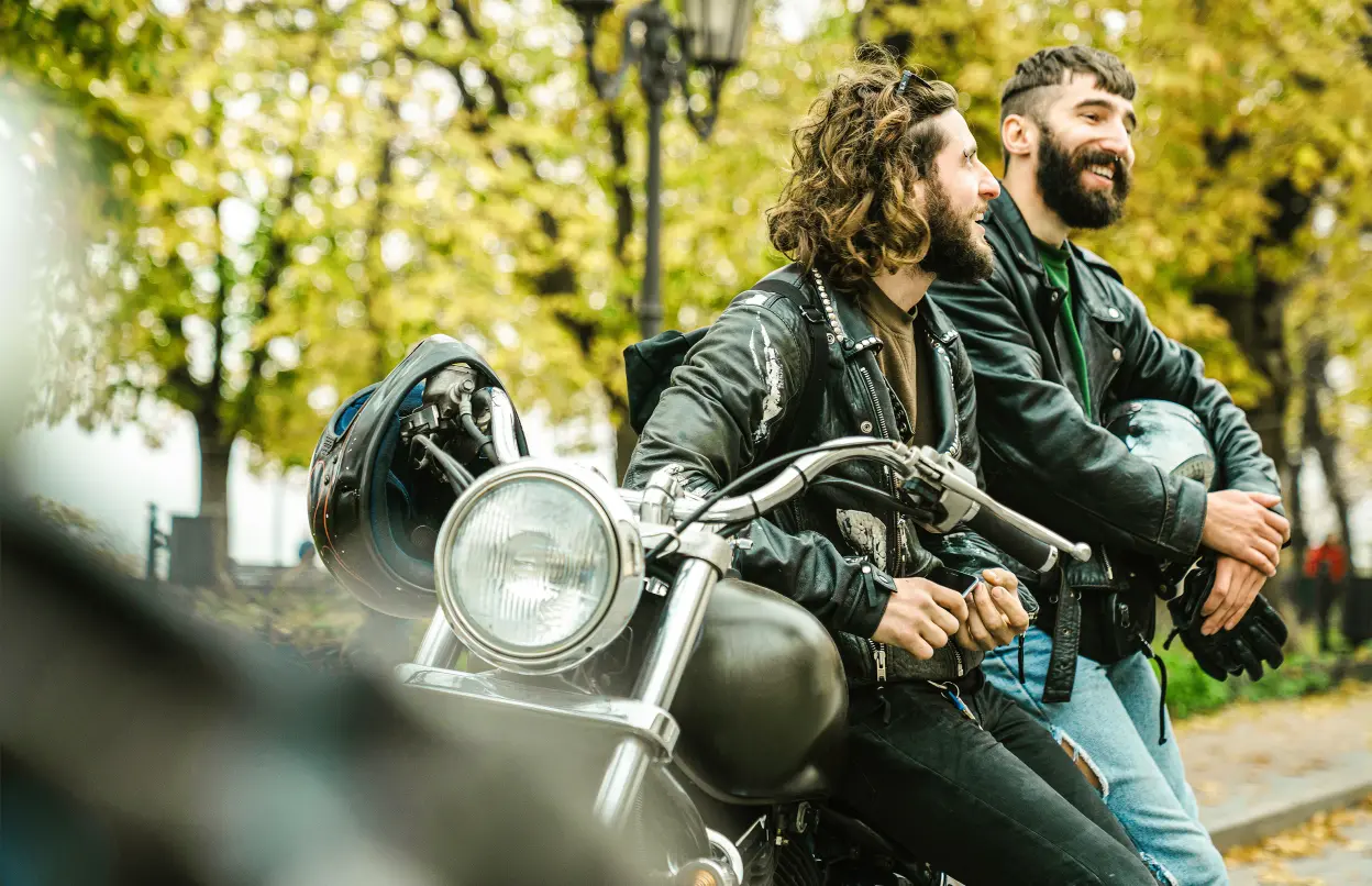 Zwei lachende Motorradfahrer lehnen an einem Motorrad.