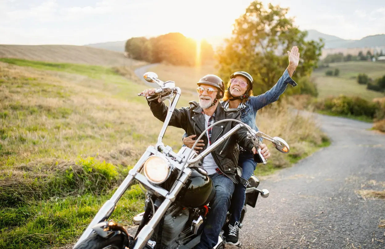 Ein lachendes Paar fährt auf dem Motorrad in der Abendsonne.